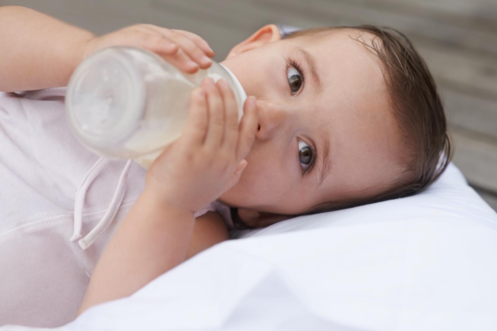 A baby, nestled comfortably on a pillow and wearing a light-colored sleeveless top, enjoys feeding time with one of the best baby bottles.